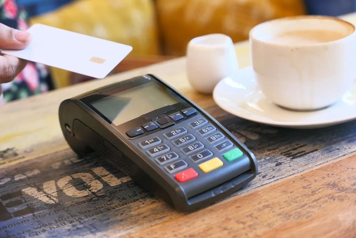Contactless card payment on a point-of-sale terminal beside a coffee cup on a café table